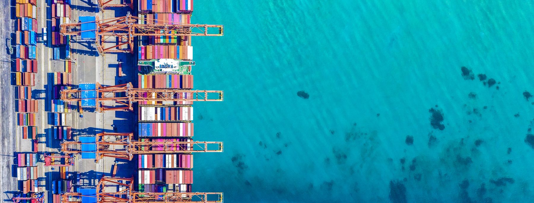 A container ship being loaded by cranes at a port, seen from above.
