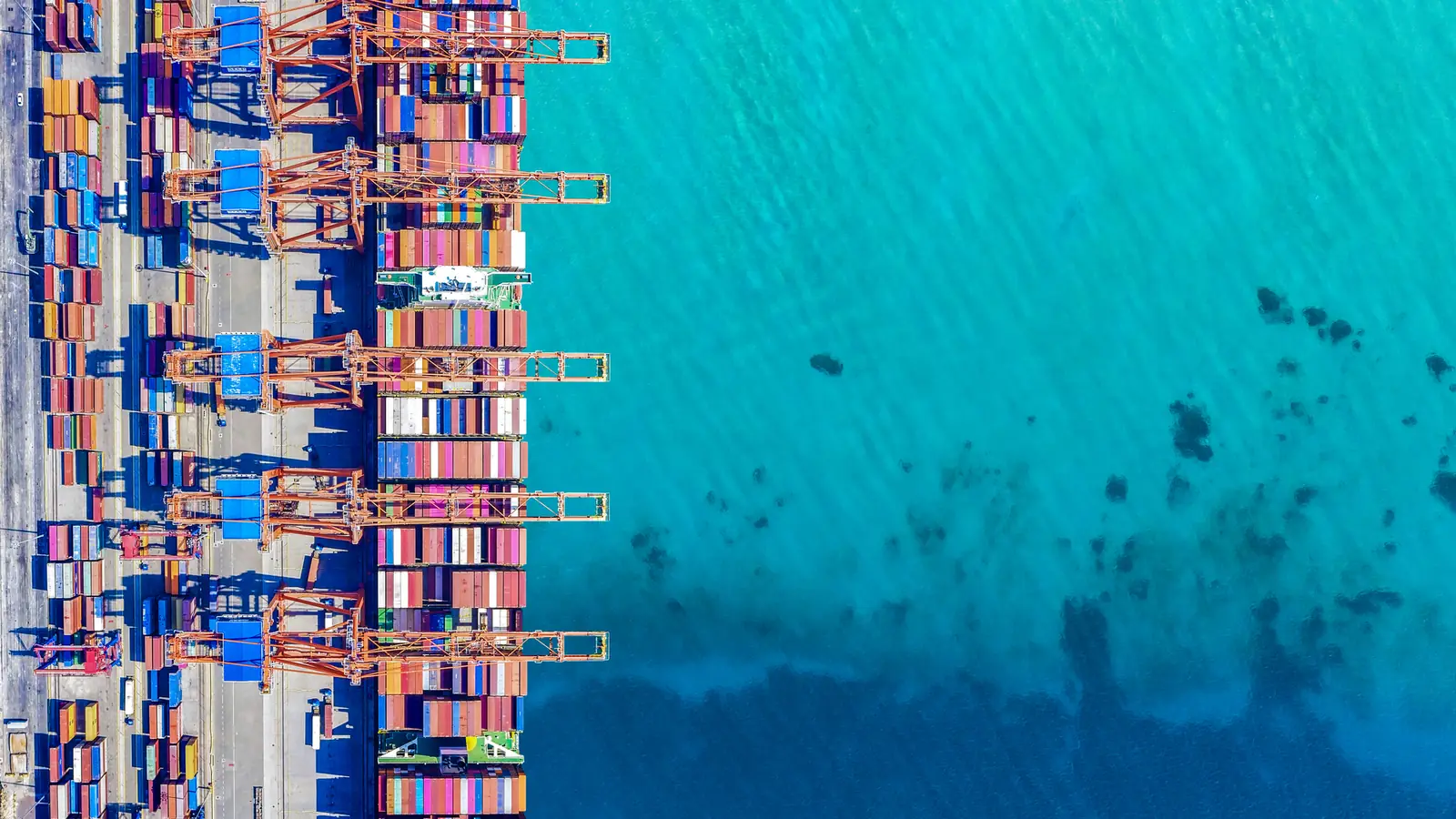 Container ships being loaded by gantry cranes at a port, seen from above.